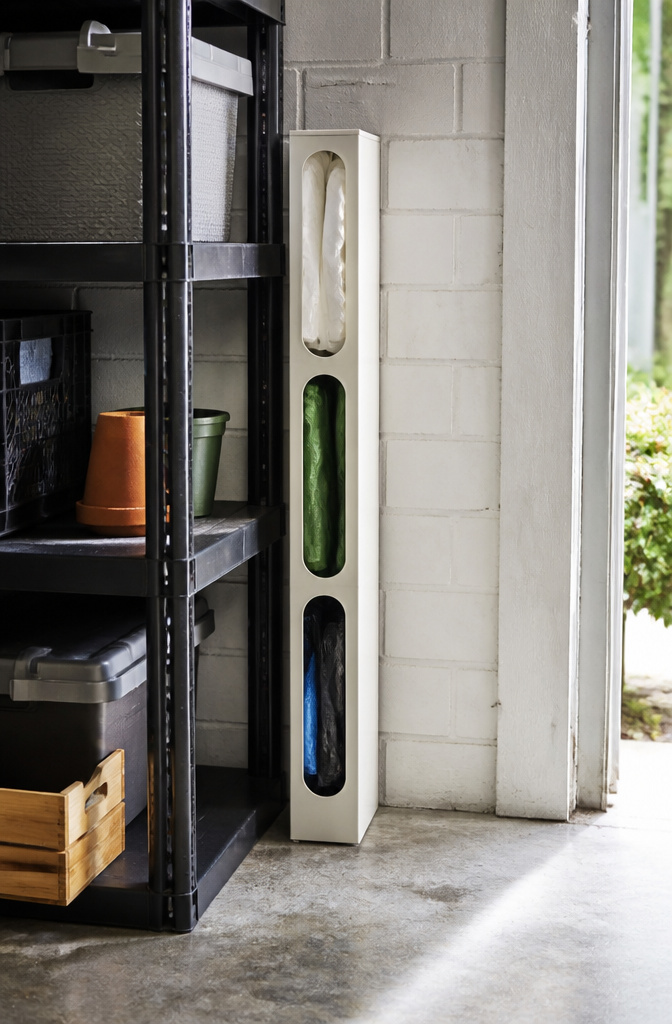 Narrow bin holding rolls of garbage bags in a garage.