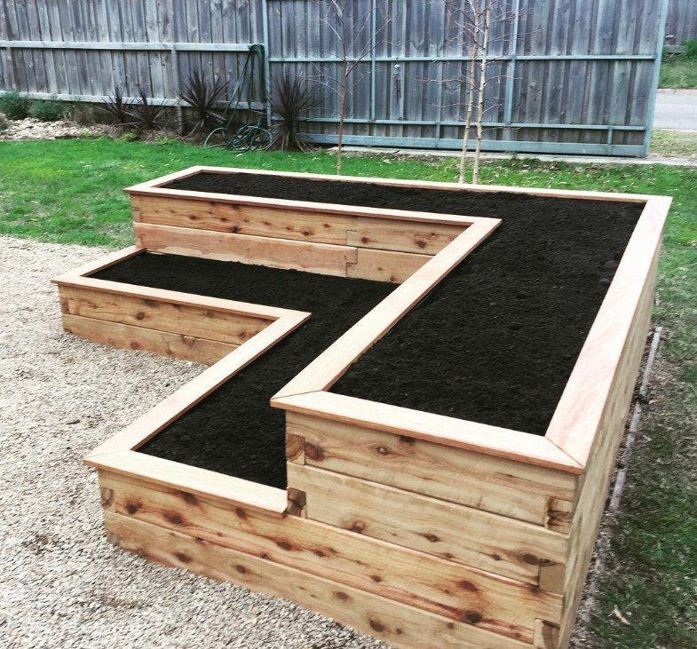 Two tier wooden planter box filled with dark soil in a backyard garden