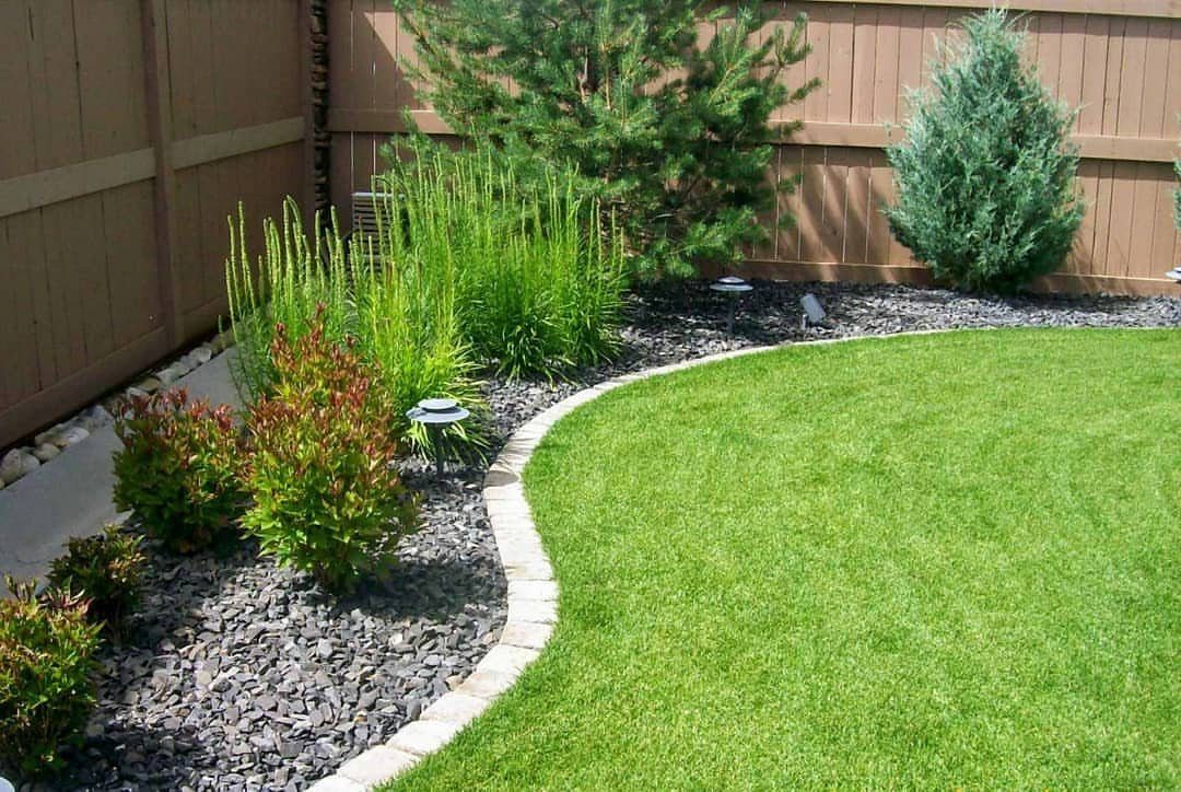 Curved green lawn with a stone border and dark rock garden bed along a fence.
