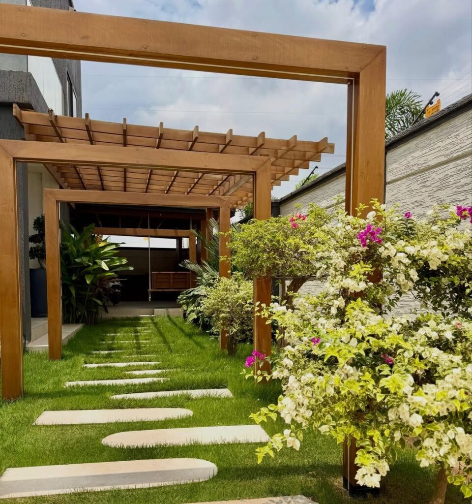 Modern front yard garden with wooden pergola, stepping stones, and flowering bushes.