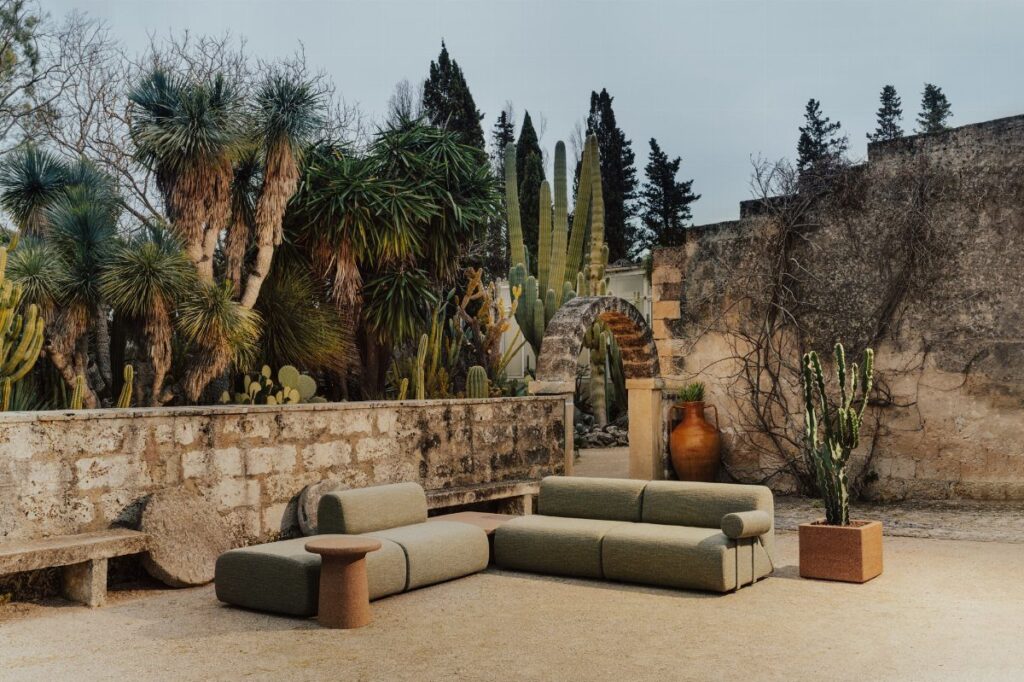 Olive green modular outdoor sofa on a sandy patio surrounded by cacti and palms.
