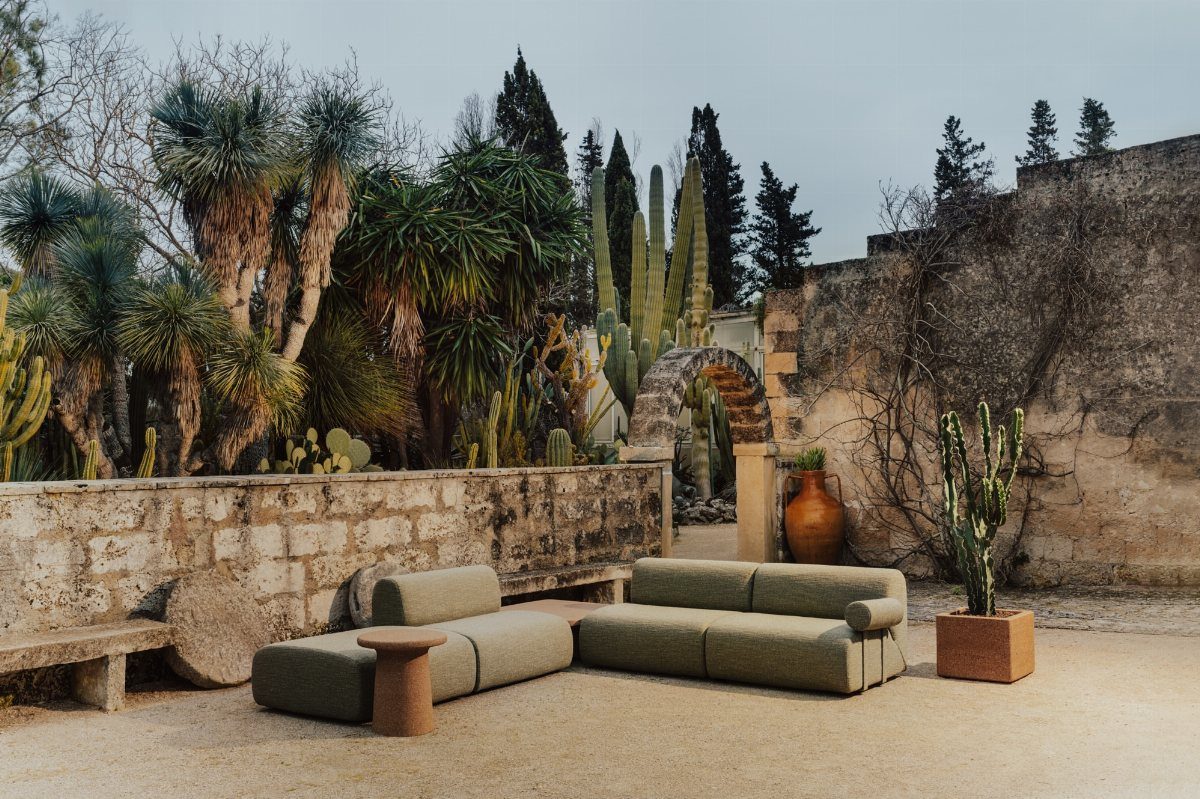 Olive green modular outdoor sofa on a sandy patio surrounded by cacti and palms.