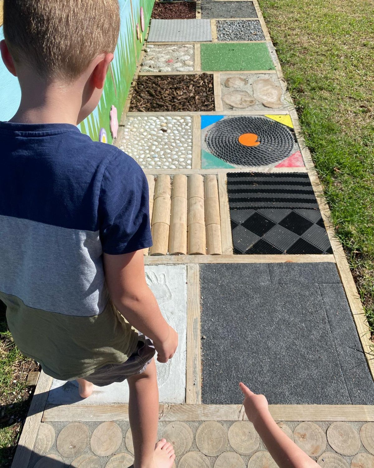 Child standing on a sensory path with various textured materials for tactile exploration.