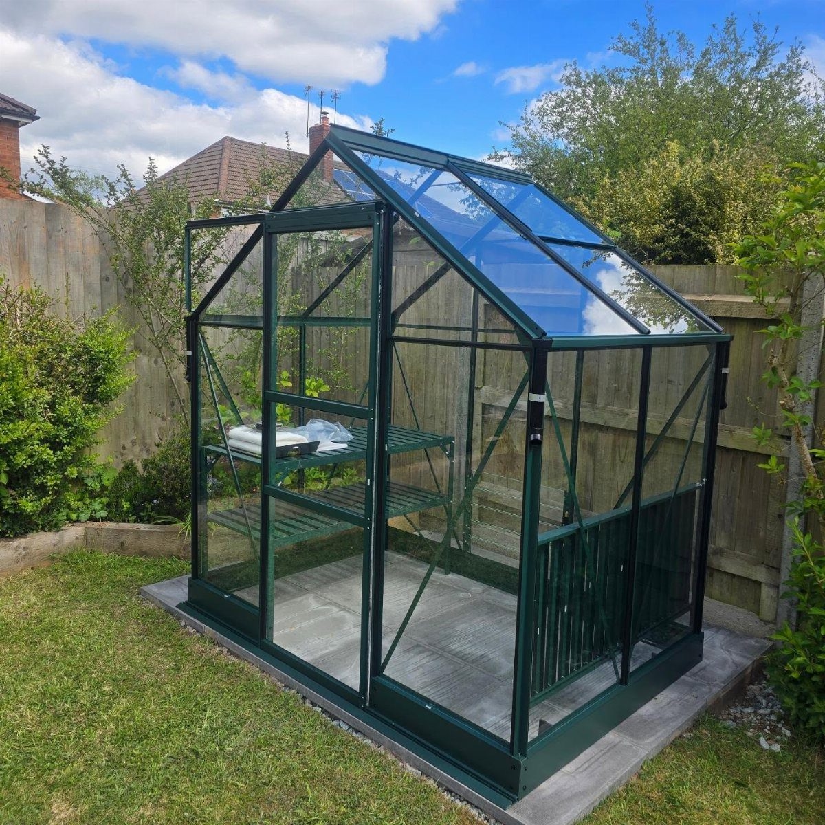 Small modern greenhouse with dark green frame and glass panels in a backyard.
